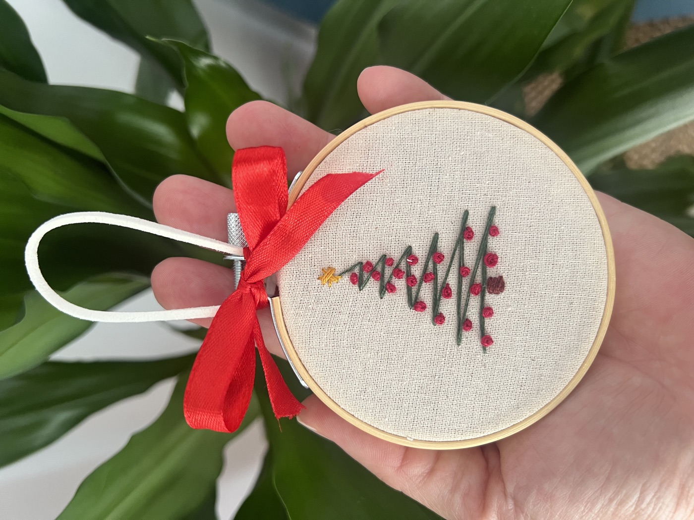 Enfeite de Natal bordado num pequeno bastidor, com árvore e laço vermelho